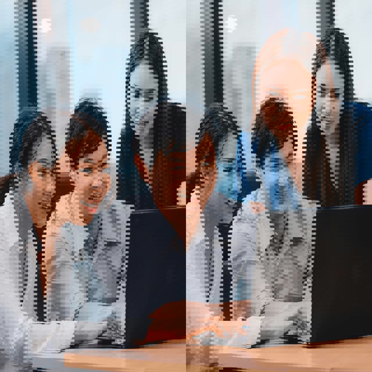 Three office workers smile with enthusiasm at a laptop screen